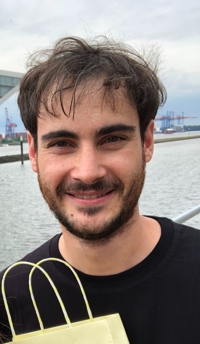Male software developer smiling in front of the water in his new home in Hamburg.